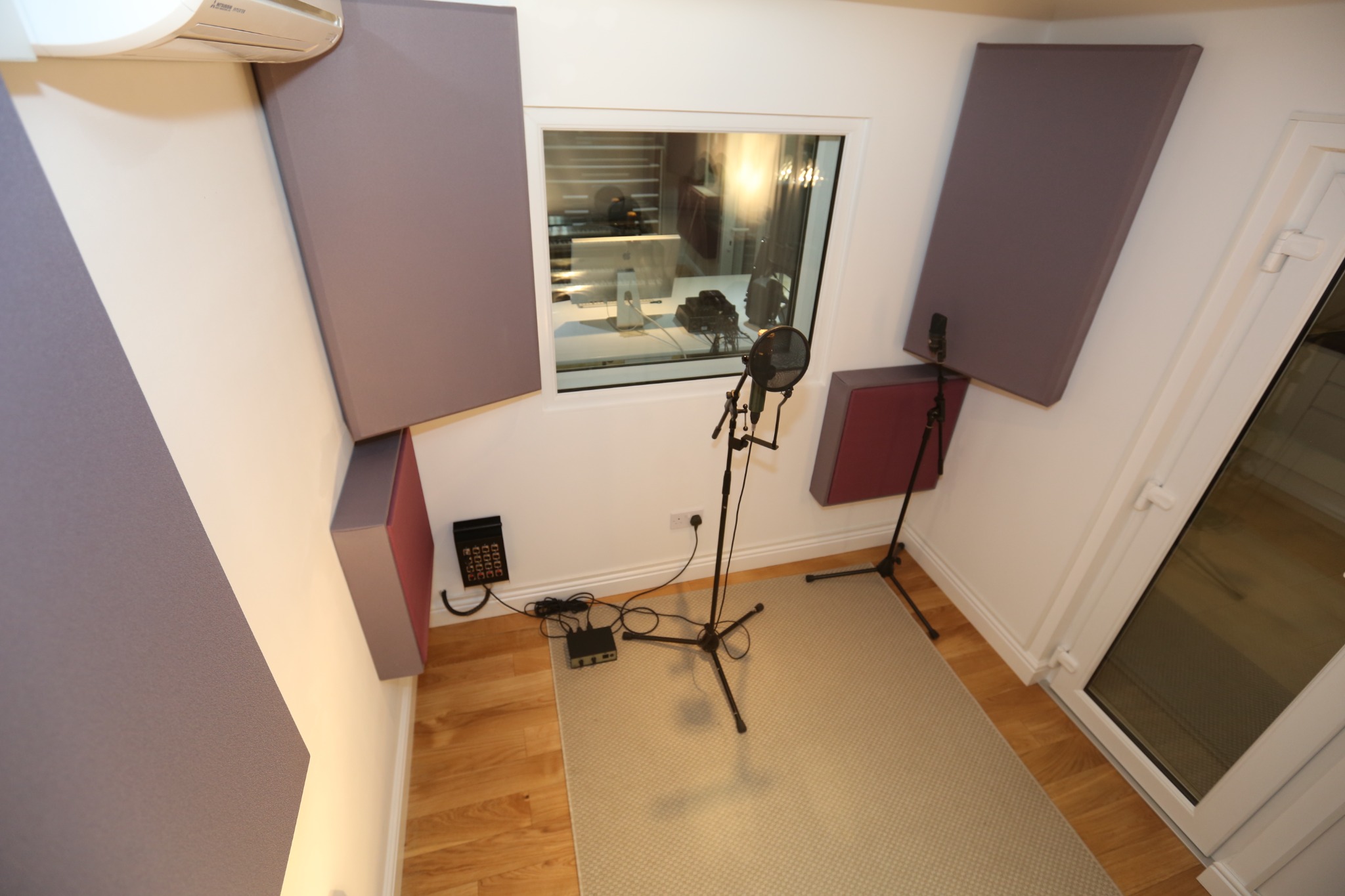 Greystoke Studio recording booth with microphones and control-room window